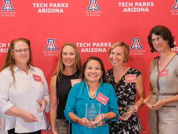 CALS faculty stand in front of a Women of Impact awards banner holding their glass awards.