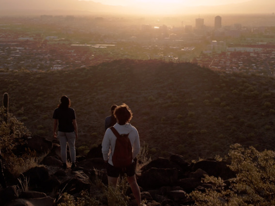a group of students stands atop a mountain at sunset looking down over the Tucson valley