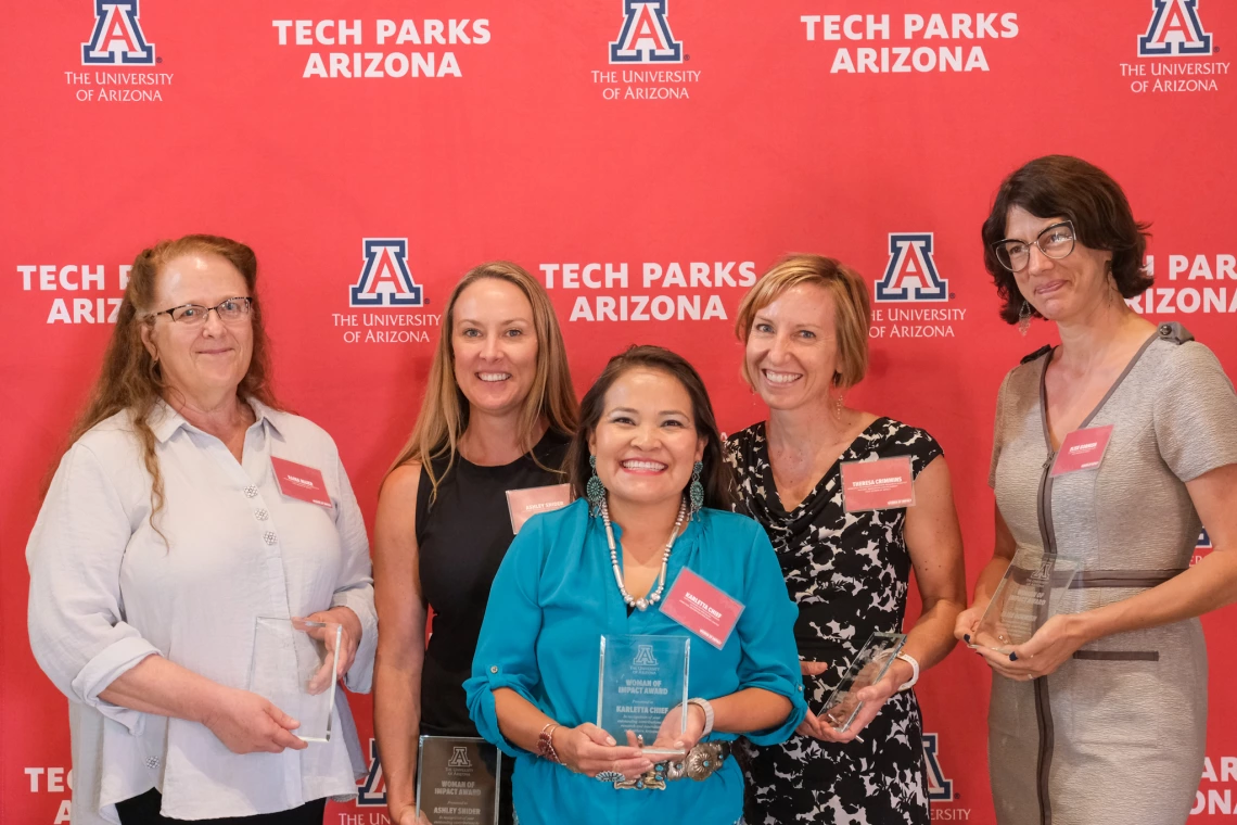 CALS faculty stand in front of a Women of Impact awards banner holding their glass awards.